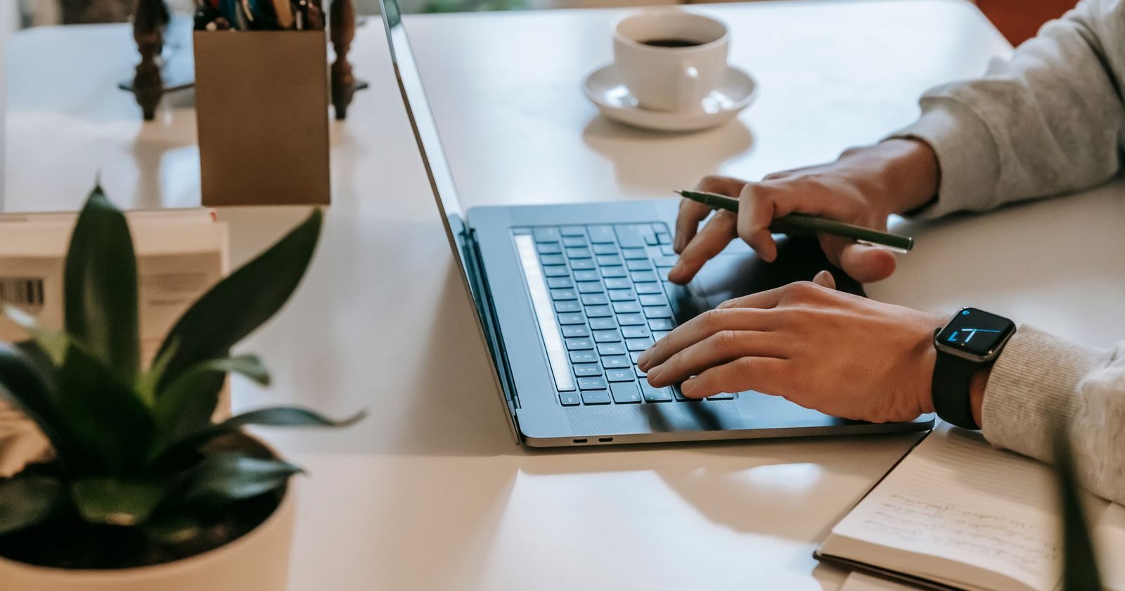 Self-employed person typing on a laptop at a desk with a coffee and notebook
